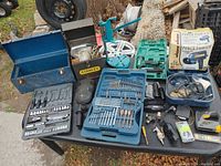 Full lot overview on black table showing toolboxes, bit sets, circular saw blades, and power tools in various cases and boxes.