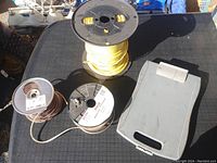 Three spools of wiring including a large yellow wire spool, two smaller copper wire spools, with a Hydro One clipboard on a black table.
