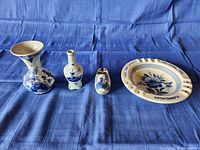 Four pieces of blue and white Dutch pottery displayed on blue fabric.