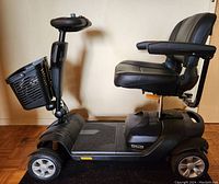 Side view of black electric mobility scooter showing tiller, front basket, deck and cushioned seat