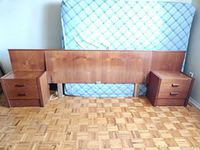 Full view of teak wood headboard with two matching nightstands, mattress in background. Floor has parquet pattern.