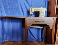 Side view showing vintage green sewing machine atop the wooden cabinet with pull-out drawer and foldable design.