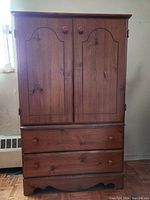 Front view of wooden wardrobe unit with two doors and two drawers, medium brown color, decorative paneling, and wooden knobs.