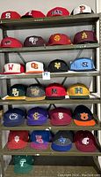 Shelving unit with rows of collegiate fitted and SnapBack hats featuring various logos and colors.
