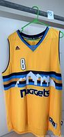 Front view of the yellow Denver Nuggets Adidas basketball jersey with Danilo Gallinari #8, hanging on a green hanger.
