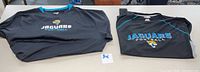Two black Jacksonville Jaguars long sleeve shirts side by side on a table, showing front logo and collar details.