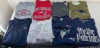 Eight New England Patriots branded shirts and polos laid out including grit and stain details