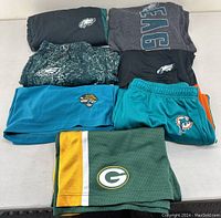 Top view of folded NFL shorts and sweatpants showing multiple teams: Eagles, Jaguars, Dolphins, Packers