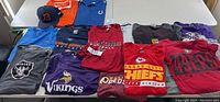 Overview of NFL apparel laid out on a table including shirts and a hat representing various teams.