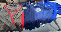 Four NHL jackets laid on table, including grey Ottawa Senators, blue Toronto Maple Leafs, and Pittsburgh Penguins jackets.