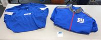 Photo of two blue New York Giants apparel pieces by Reebok: pullover and full zip jacket laid flat on a table.