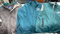 Wide view of three Philadelphia Eagles NFL jackets and vest side by side on a table showing zip-up jackets with collars and reversible vest.