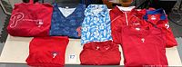 Group of Phillies apparel items laid out including hoodies, pullover tops, scrubs, Hawaiian style shirt, and shorts.