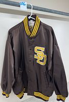 Brown San Diego Padres snap front jacket with striped cuffs, collar, and waistband, hanging on hanger.