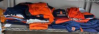 Shelving with various Syracuse college apparel items including folded jackets, shirts, and hats in Syracuse orange and navy blue colors.