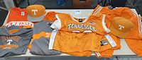 Photo of assortment of Tennessee Vols apparel including two caps, replica jerseys, and shirts, primarily orange and gray.