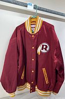Front view of maroon snap front jacket with striped ribbed collar, cuffs, and waistband, featuring Washington Redskins 'R' patch with feather.