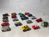 Overview of 20 small toy cars laid out showing different styles and colors under white background.