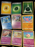 Photo showing Basic Lightning Energy, Basic Grass Energy, and Shining Grass Energy cards on top row; various Pokémon cards including Sobble, Hatterene, Gligar, Exeggcute, Togepi, Munna below