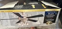 Photo of the boxed 52 inch Plaza ceiling fan showing product branding and features on box.