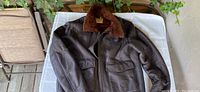 Brown leather bomber aviator flight jacket with shearling collar laid flat showing full front view, zipper, and pockets.