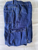 Folded view of blue denim cargo jeans showing main body, multiple pockets, and denim color texture.