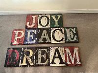 Front view of three wooden plaques with distressed paint spelling JOY, PEACE, DREAM.
