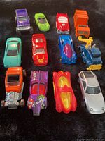 Overview of all 12 diecast Hot Wheels cars arranged on a surface showing variety in color and model type, including Joker purple car, vintage styles, and McDonald's themed cars.