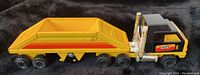 Photo of the black and yellow Tonka truck cab connected to a yellow dump-style trailer with orange and red stripes on a black background.