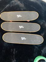 Three Tech Deck finger skateboards viewed from the top showing black grip tape and logo
