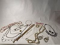 Overview photo of vintage costume jewelry including multiple necklaces, bracelets, and earrings in various colors and materials such as faux pearls, pink beads, metal chains.