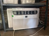 White Frigidaire window air conditioner sitting on floor shelf.