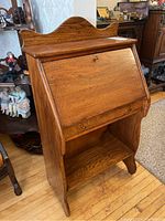 Front view of antique children's wooden writing desk with fold-down desktop closed, drawer below, and lower shelf.