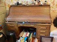 Front view of antique wooden roll-top secretary desk showing eleven drawers, lockable roll-top cover partially open with papers stored underneath, surrounding items not included.