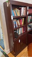 Front view of the wood veneer bookcase filled with books, showing three main shelves and closed double-door cabinet at bottom.