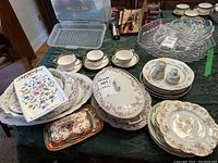 Photo showing multiple assorted china plates and serving dishes with floral patterns in soft colors, including cups and saucers
