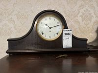Front view of wooden mantel clock showing round clock face with Arabic numerals and winding key in front.