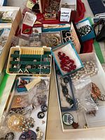 Wide view of the full lot spread out on a table showing multiple open boxes with various costume jewelry including pearl necklaces, brooches, earrings, and pins.