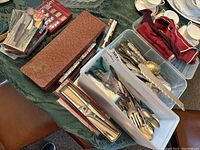 Overview of assorted cutlery including spreaders, carving set, serving spoons and forks in storage containers and boxes.