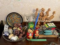 Wide view of the lot showing painted plates, candleholders, blue candles, crystal glasses, and various decorative eggs and dolls.