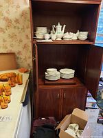 Johnson Brothers dishes displayed on wooden shelving unit and in cardboard boxes including cups, plates, bowls, coffee pot, and pitchers.