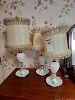 Three vintage-style table lamps with white hobnail milk glass bases and decorative fabric lamp shades photographed on a wooden surface.