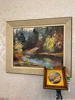 Both framed items together showing the landscape painting and smaller round print on a wall.