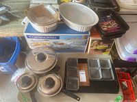 Photo showing two white Corningware casserole dishes with lids on top of original Corningware box, three stainless steel pots with black handles and lids, glass divided serving dishes, and black metal roasting pan.