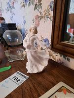 Front view of Royal Doulton figurine showing face, torso, and flared skirt on wooden surface with background floral wallpaper.