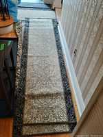 Top view of a machine made runner carpet with beige floral pattern and blue border along a wooden floor and wallpapered wall