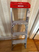 Full view front of aluminum step ladder showing three steps and red top.