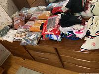 Full view of dresser top with stacked sweaters and t-shirts in multiple colors, some in clear plastic bags