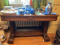 Front view of the vintage wooden table with two drawers, showing the wood grain texture and cylindrical supports.