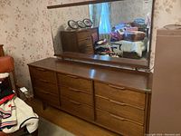 Front view of teak dresser with nine drawers and matching mirror in bedroom setting